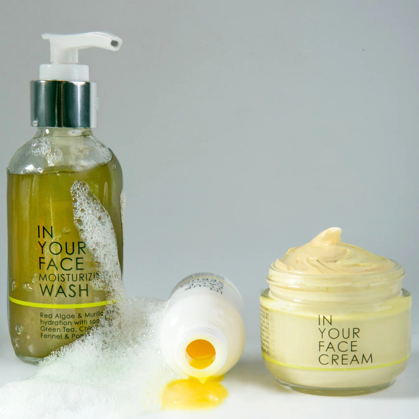 Skincare products including a bottle of 'In Your Face Moisturizing Wash' and a jar of 'In Your Face Cream' on a gray background.
