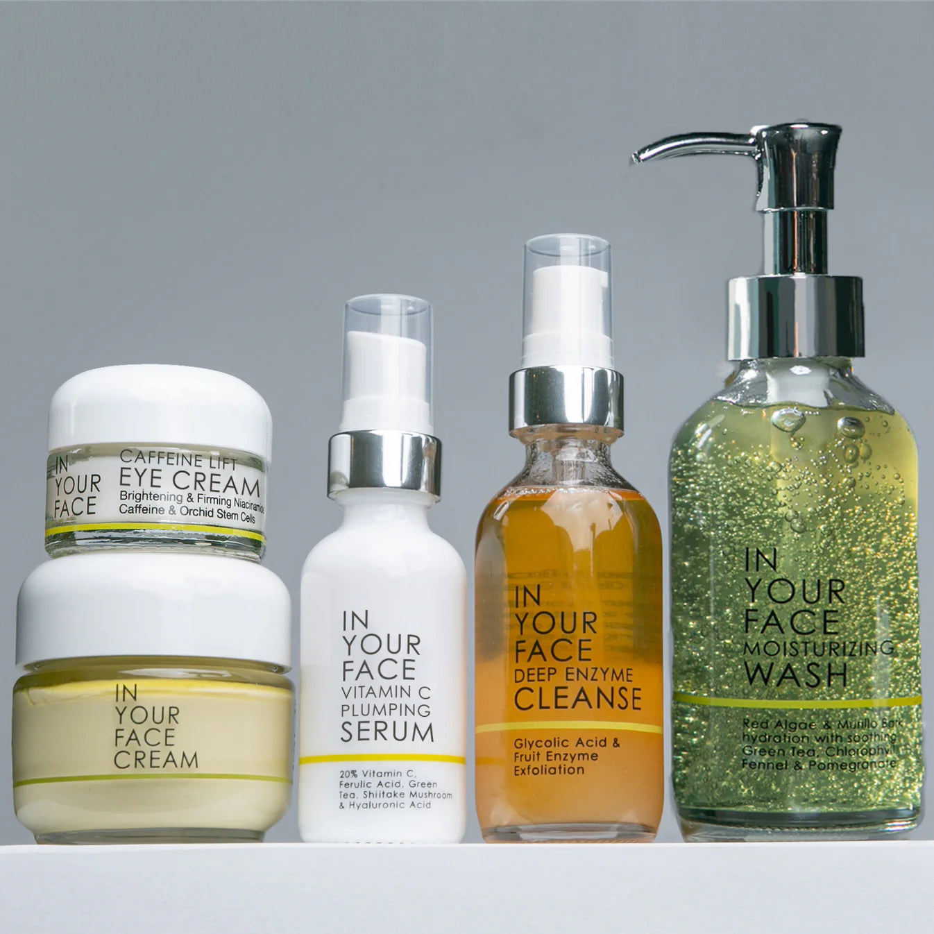A collection of skincare products including a moisturizing wash, vitamin c plumping serum, caffeine lift eye cream, the cream, and deep enzyme cleanse, displayed on a white surface.