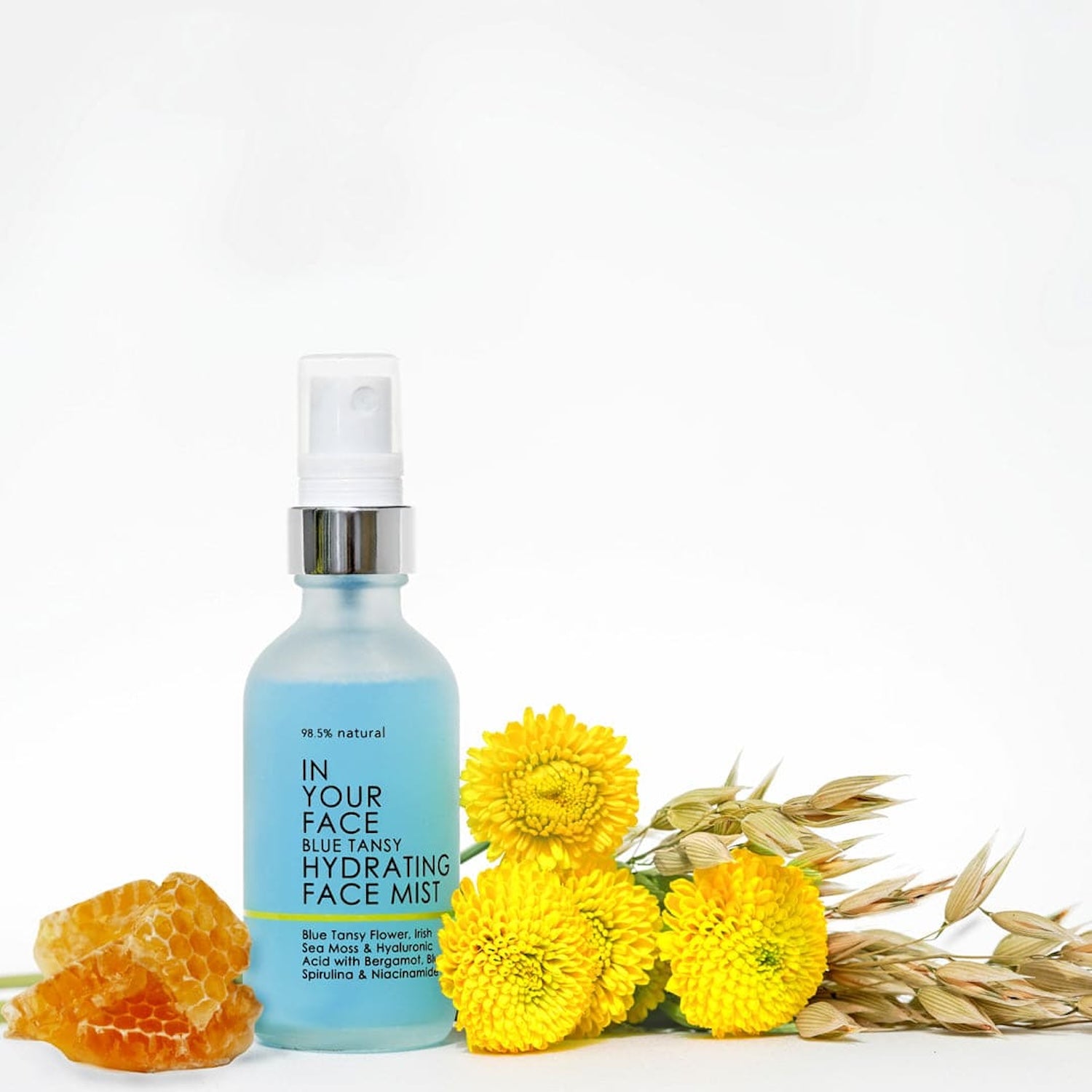 In Your Face Blue Tansy Hydrating Face Mist displayed with natural ingredients, including honeycomb and vibrant yellow flowers, highlighting its nourishing botanical blend.