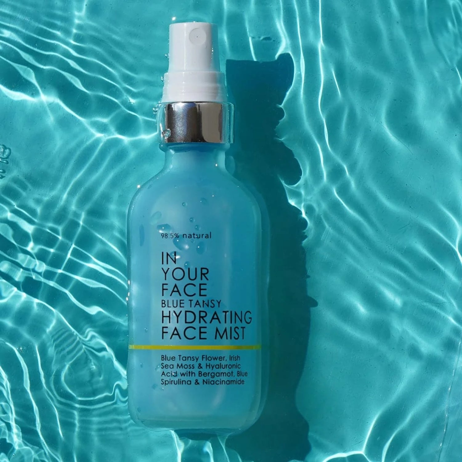 Blue Tansy Hydrating Face Mist by In Your Face floating in shimmering blue water, symbolizing its hydrating and refreshing properties.