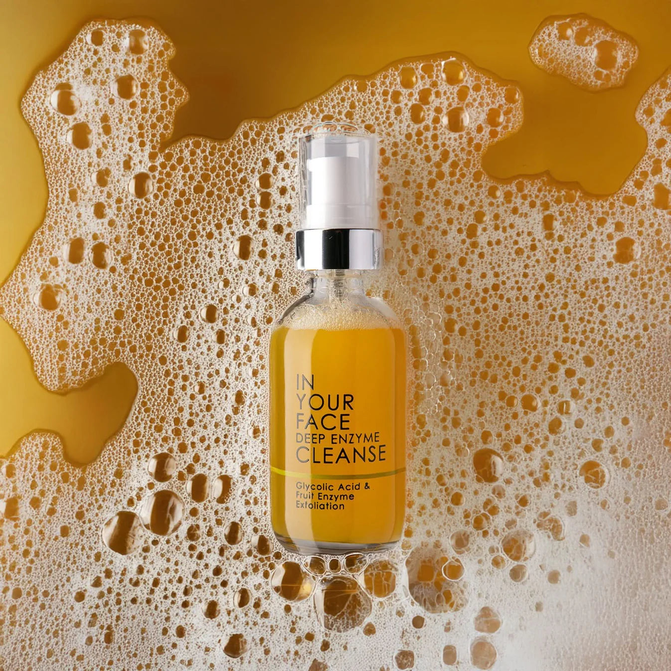 Skincare serum bottle labeled 'In Your Face Deep Enzyme Cleanse' on a textured yellow background with bubbles.
