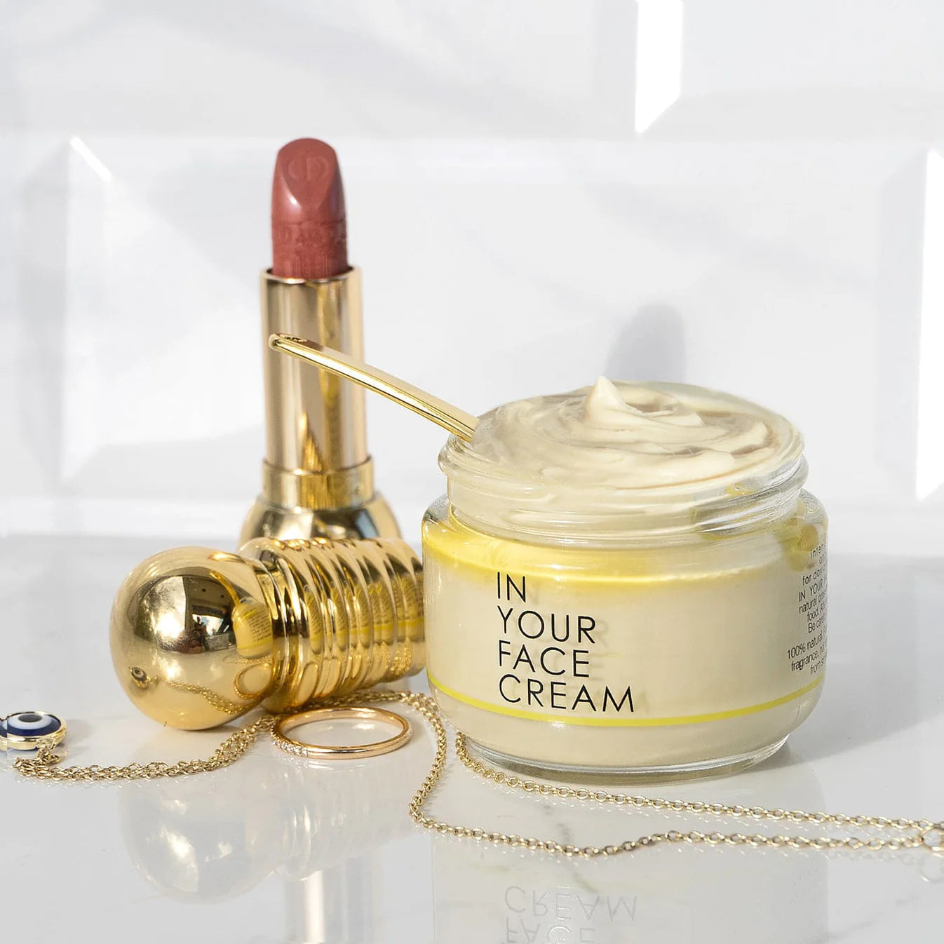 In Your Face Cream jar with gold spatula, luxury lipstick, and jewelry – hydrating face moisturizer for radiant skin