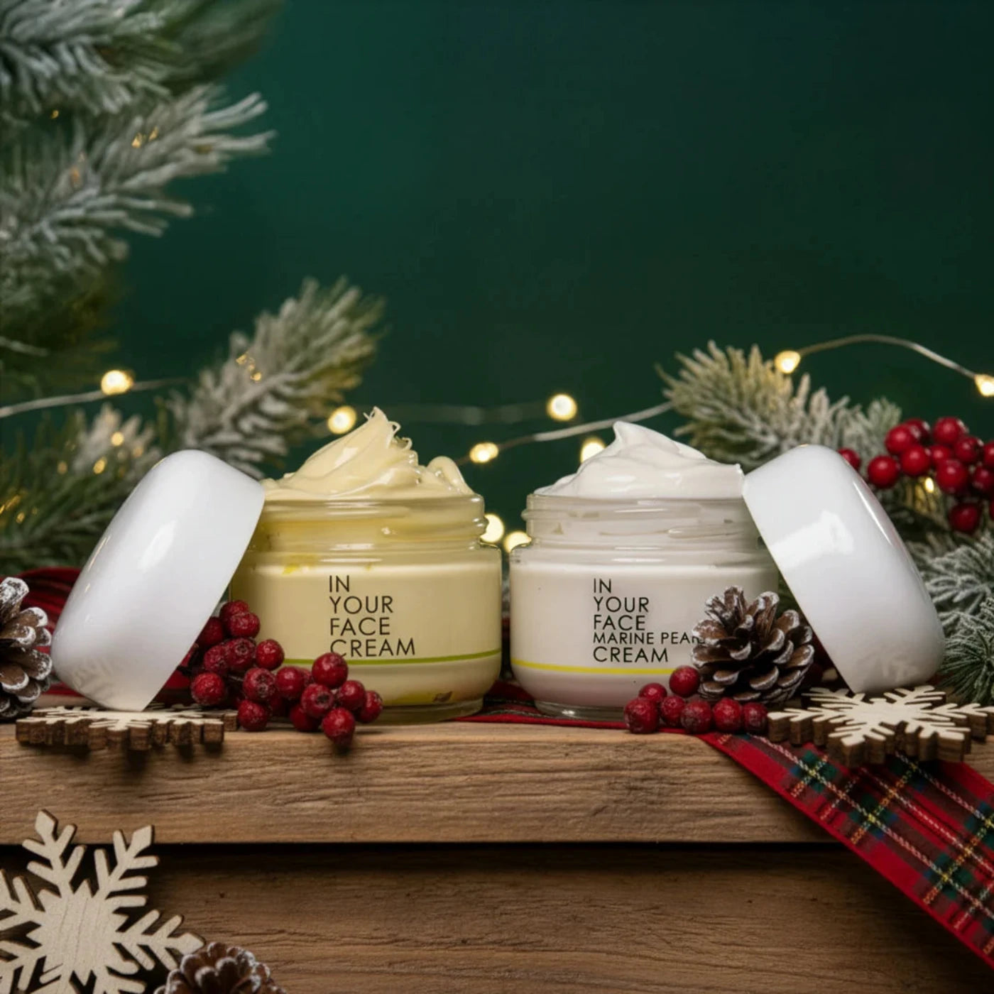 Cosmetic jars labeled 'In Your Face Cream' on a wooden tray with Christmas decorations.