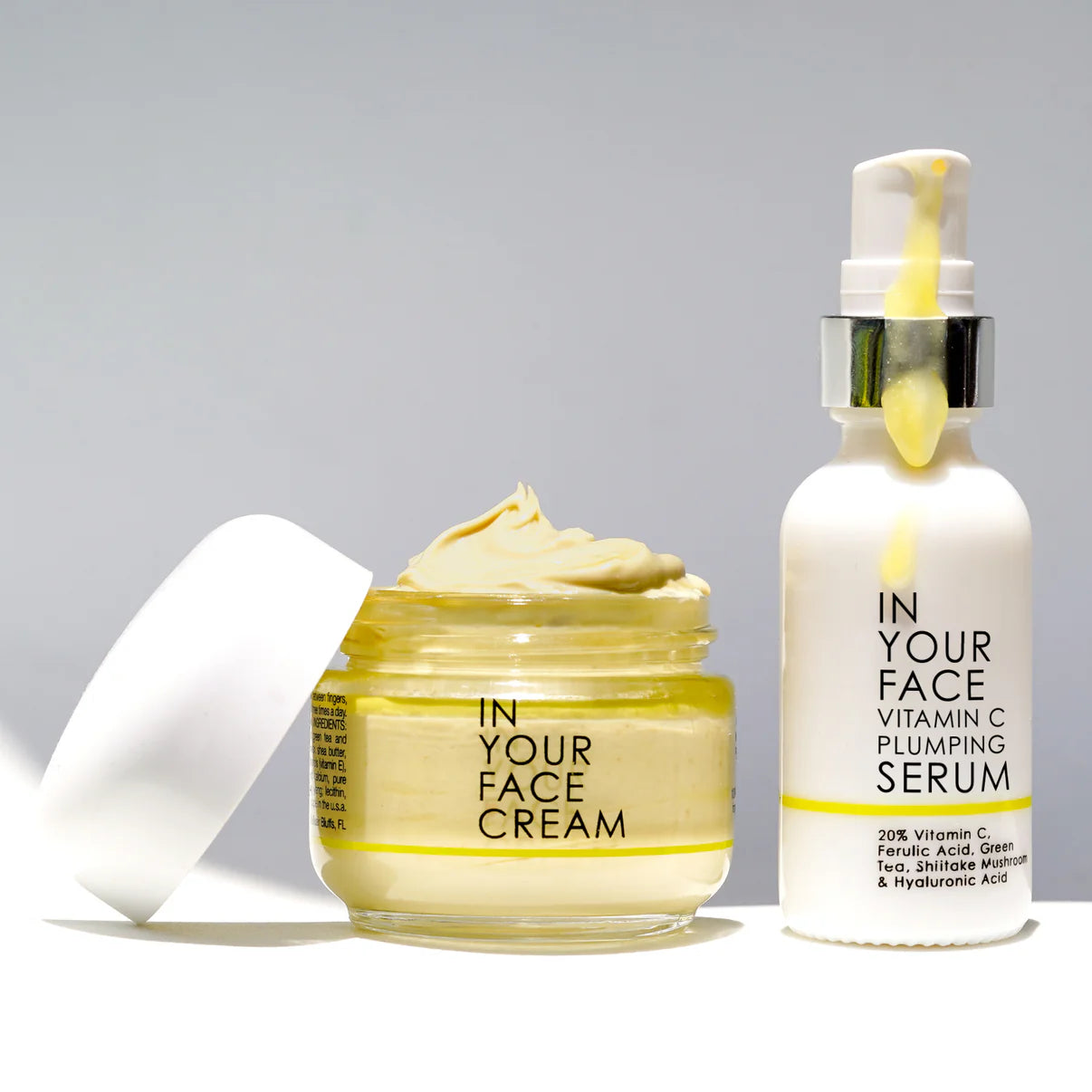 Skincare products 'In Your Face Cream' and 'Plumping Serum' on a gray background