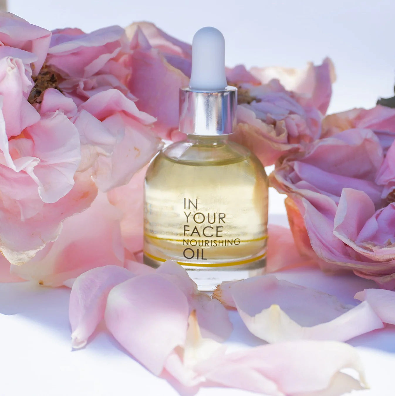 In Your Face Nourishing Oil bottle surrounded by soft pink rose petals – hydrating and glow-boosting face oil