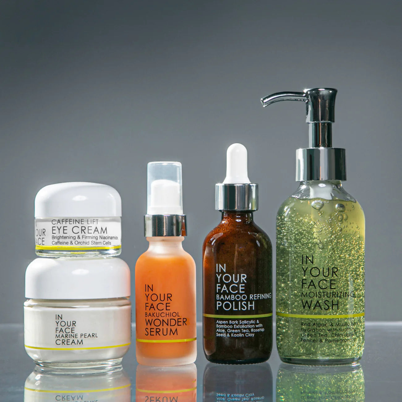 Set of facial skincare products on a reflective surface with a gray background