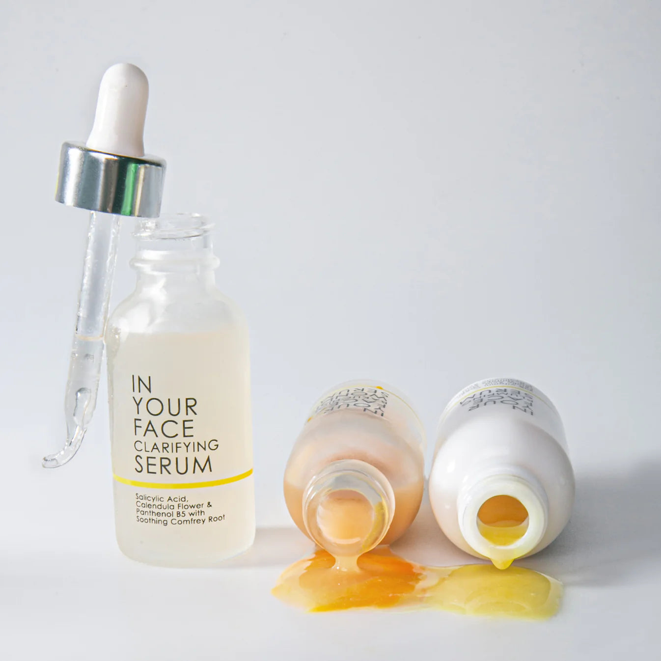 Serum bottle with dropper and two open bottles showing yellow liquid on a light gray background