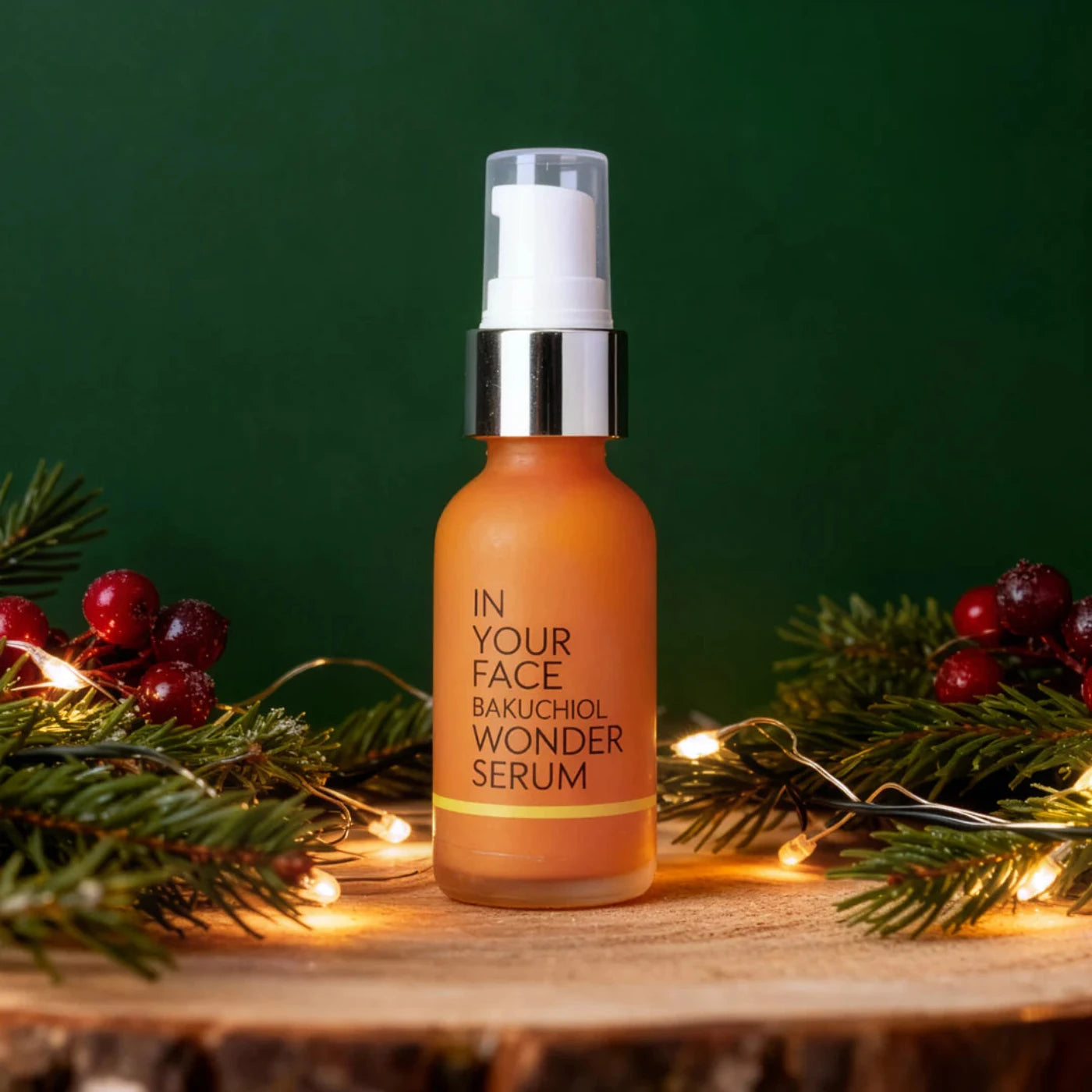 Bottle of 'In Your Face Bakuchiol Wonder Serum' with decorative greenery and lights on a wooden surface.