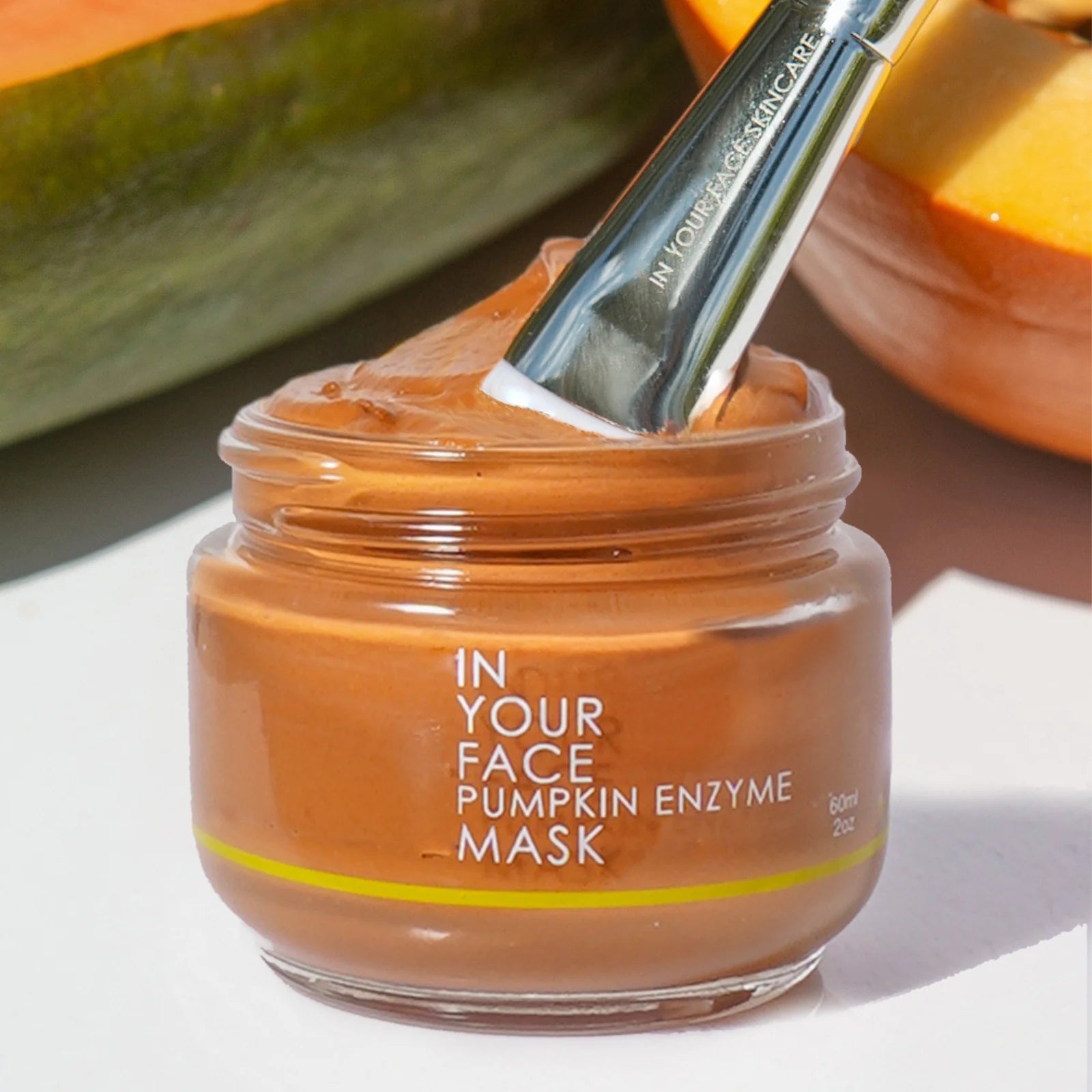 Jar of pumpkin enzyme mask with a brush on a white surface