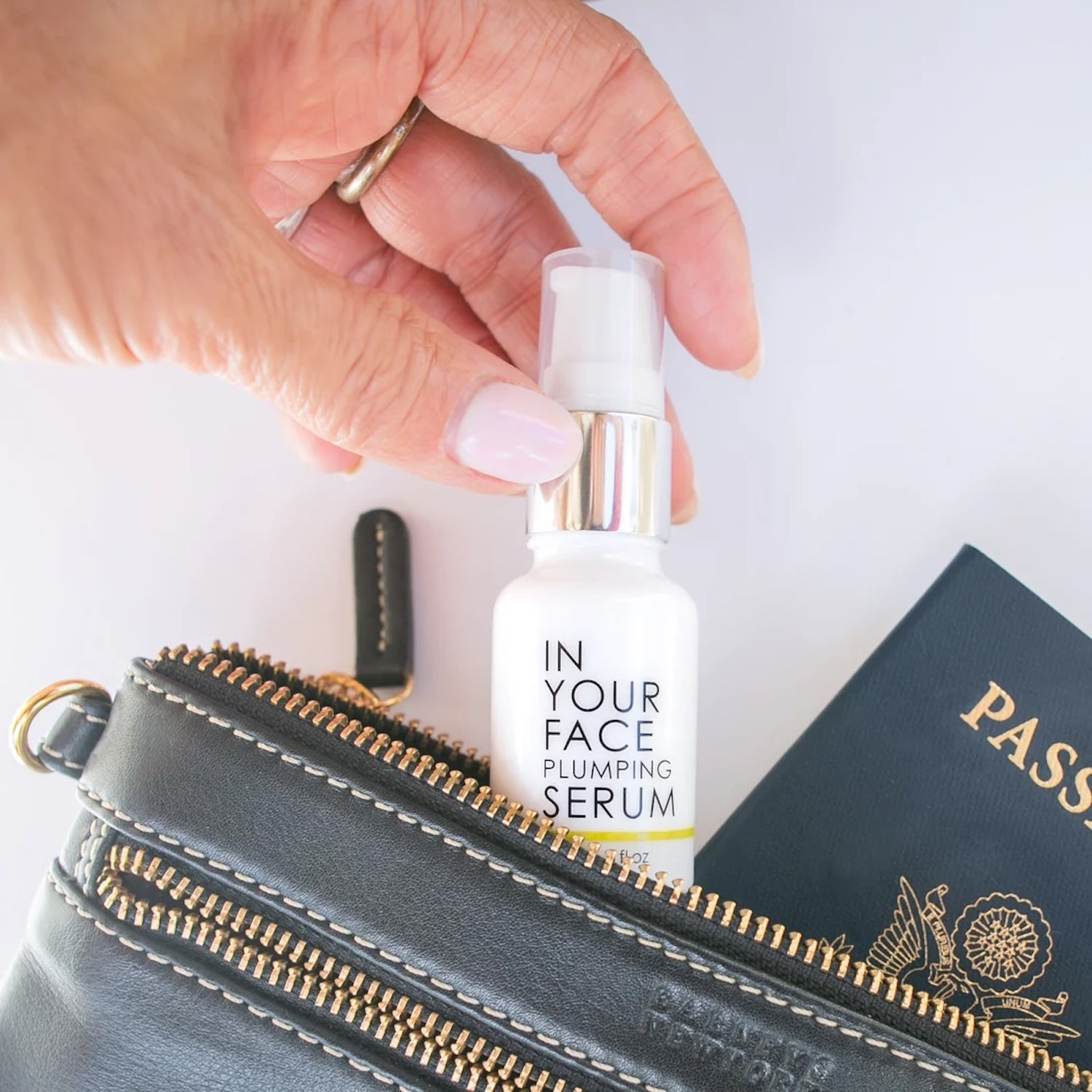 In Your Face Vitamin C Plumping Serum Mini being placed in a travel pouch with a passport, highlighting its portable, TSA-friendly size.